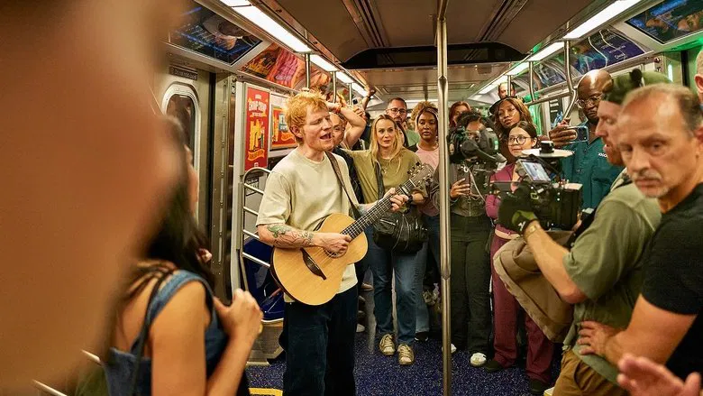 Ed Sheeran walking through a crowded NYC street with guitar on back